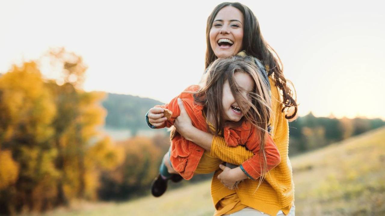 Mom holding toddler outside in the fall. Both are laughing and smiling.