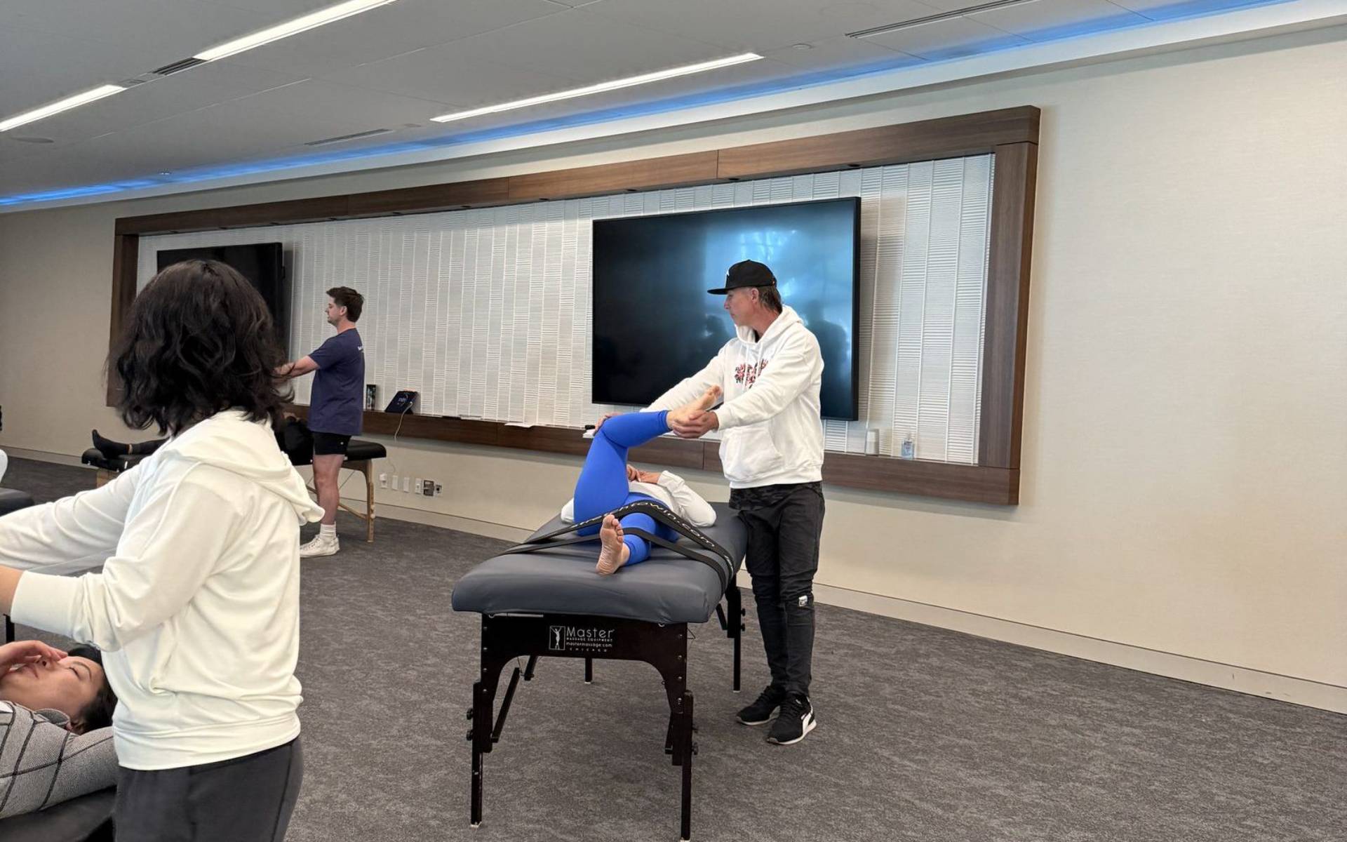 An instructor demonstrating a fascial stretch sequence while students practice on tables