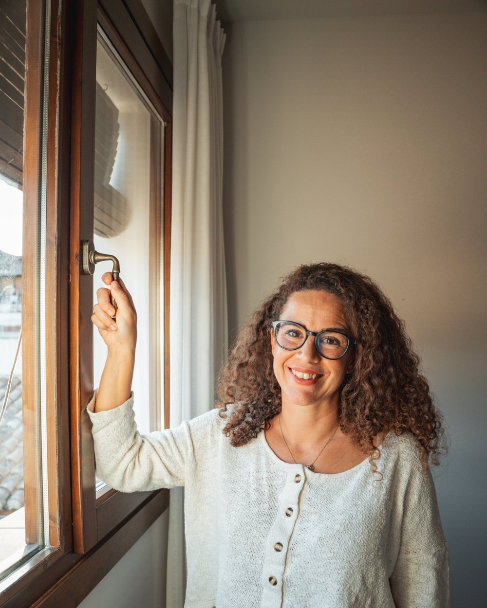 Carmen abriendo una ventana de madera a la luz natural
