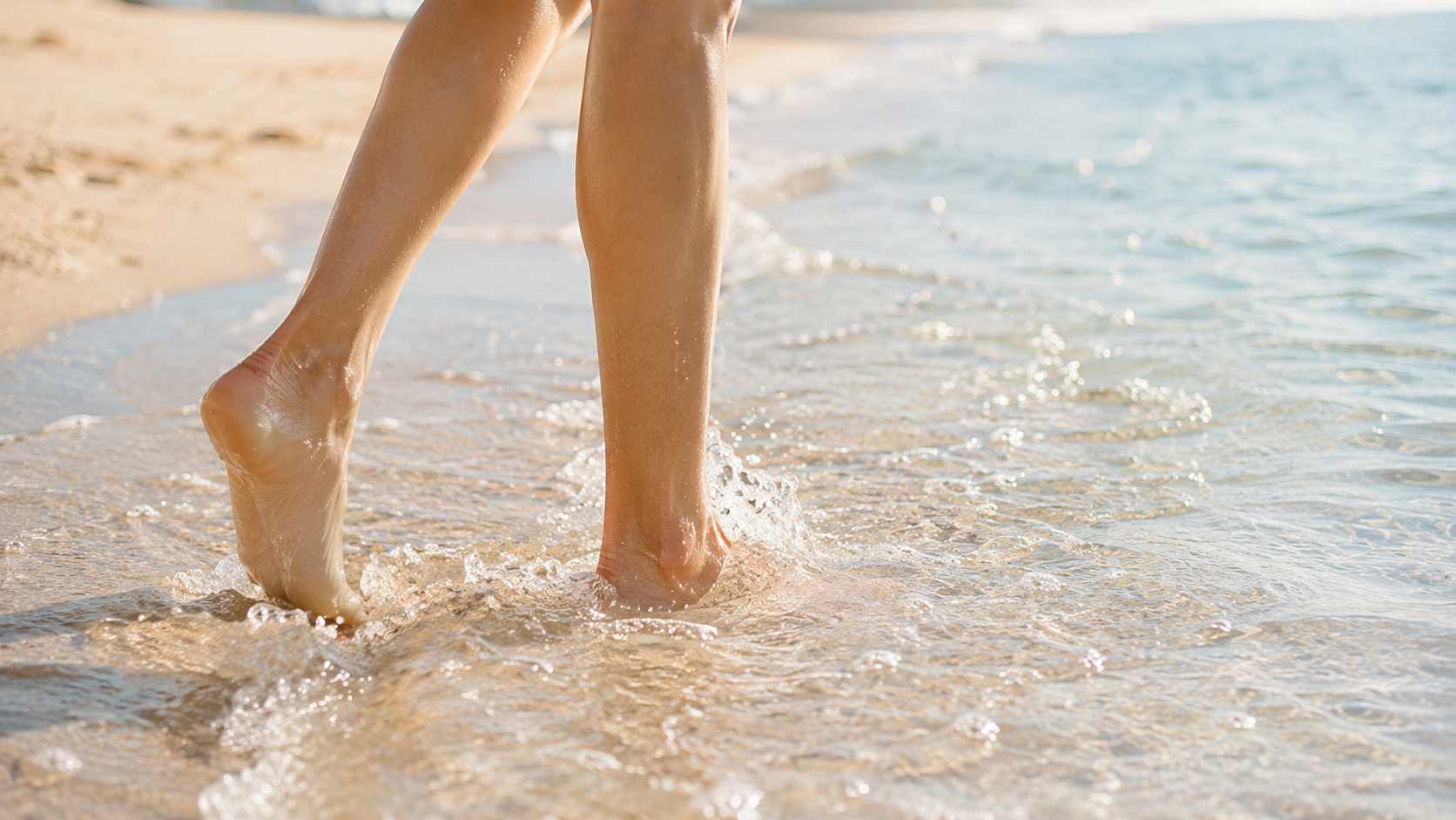 Leggerezza — i piedi nell'acqua Gambe e piedi nudi di una donna che cammina nell'acqua bassa del mare in una mattina d'estate