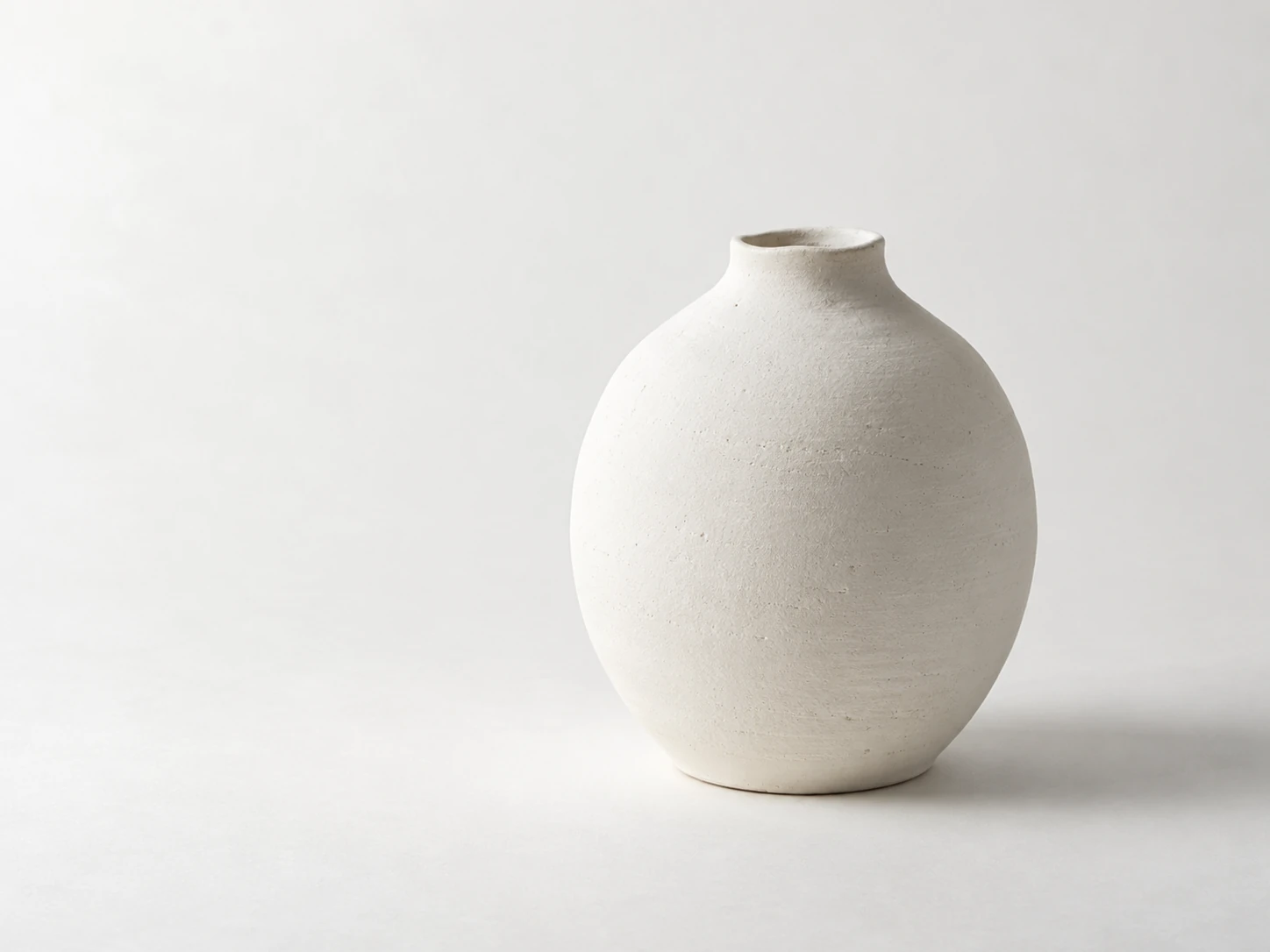 Pale matte ceramic vessel in natural side light against an off-white background