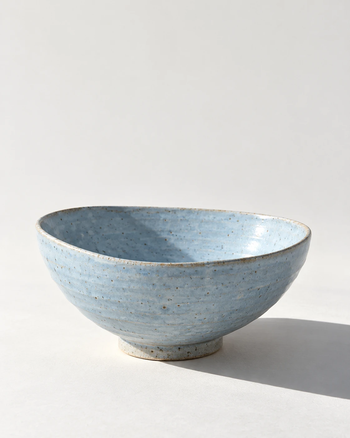 Pale blue ceramic bowl with a defined afternoon window shadow