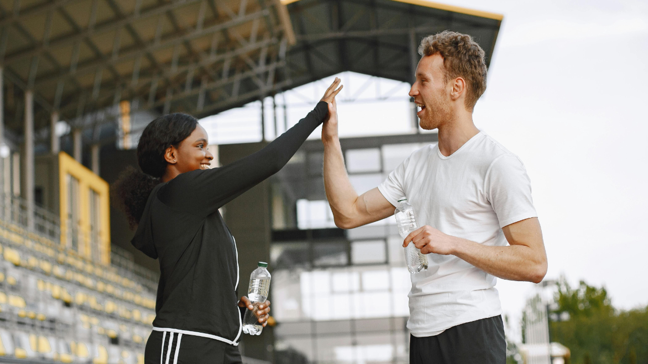 Couple in activewear high-fiving on a race track while exercising together, symbolizing healthy marriage connection and shared activities.