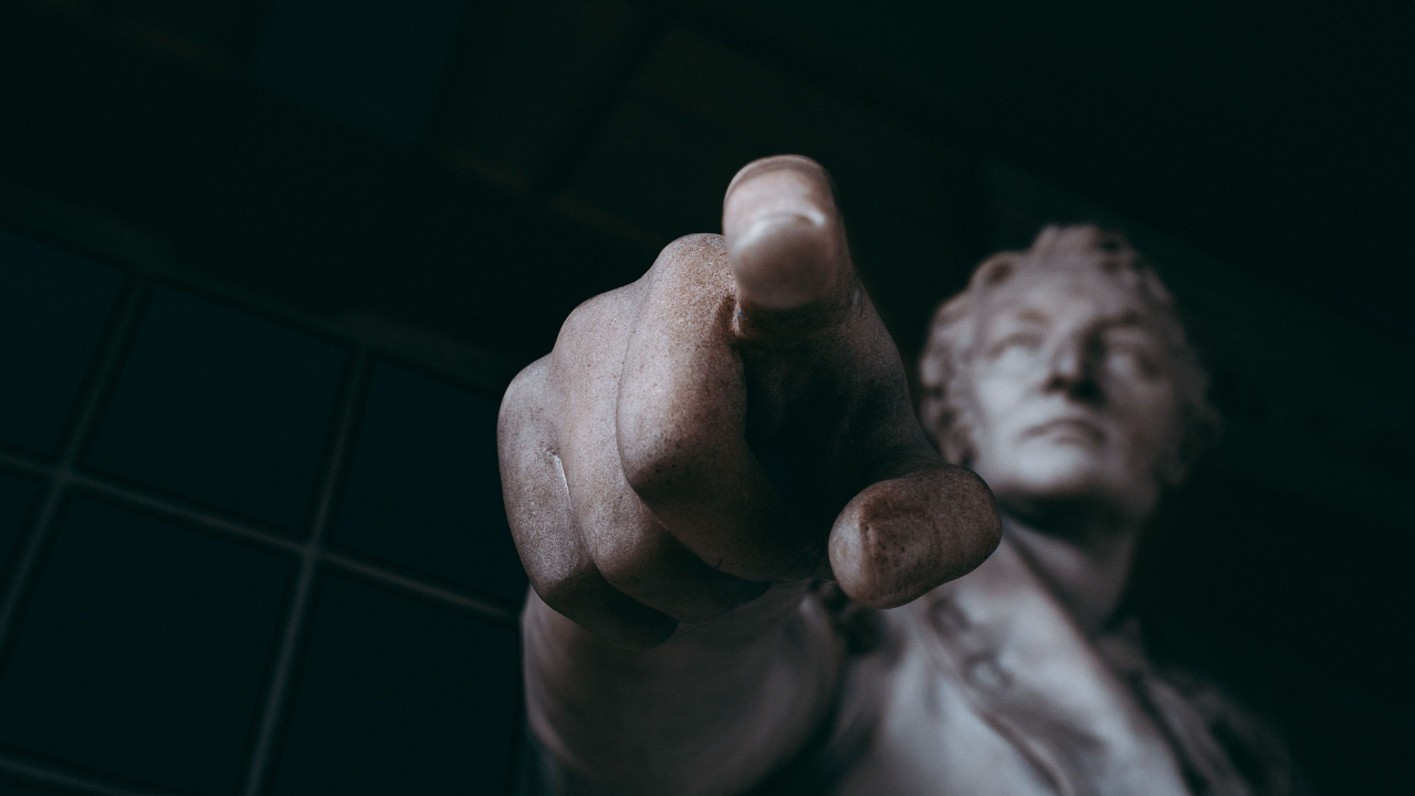Marble statue of a man pointing toward the viewer, creating the impression of judgment or criticism.