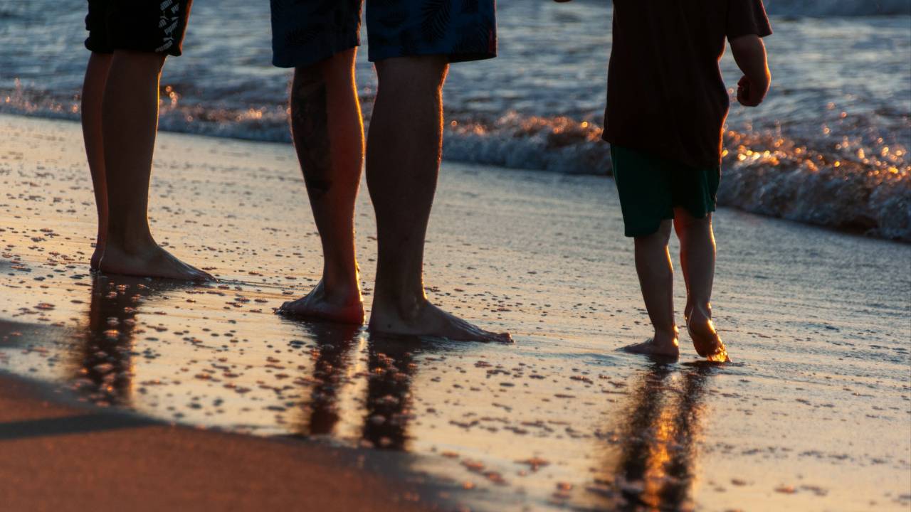 Man and toddler standing at the water’s edge on a beach.