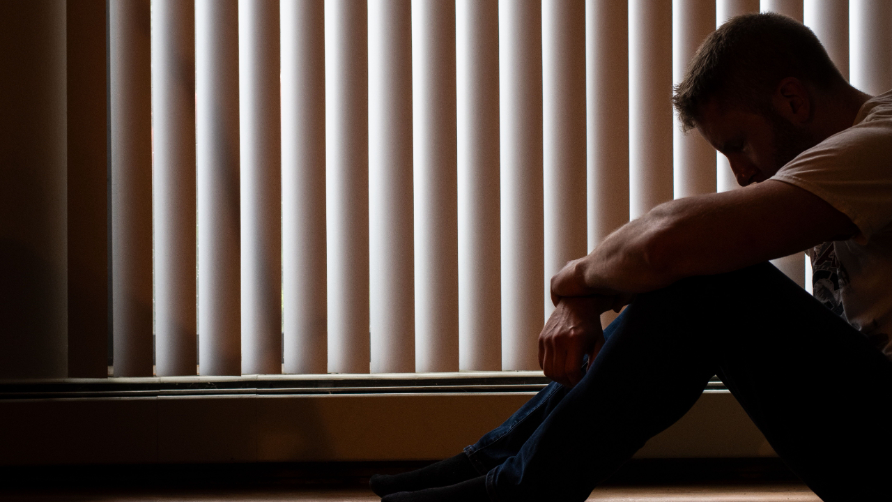 Man sitting with his head down beside a window, illustrating emotional restriction and self-reflection.