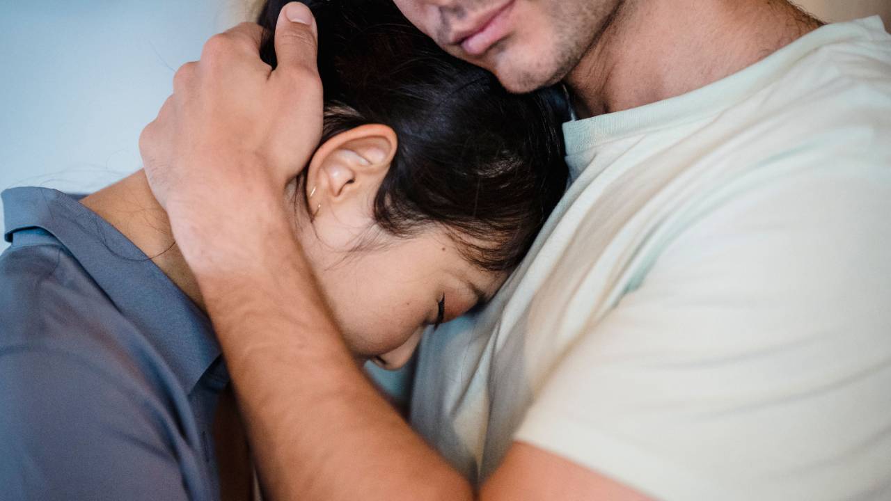 A man embracing a woman against his chest, with his face out of view and most of hers obscured by his arm.