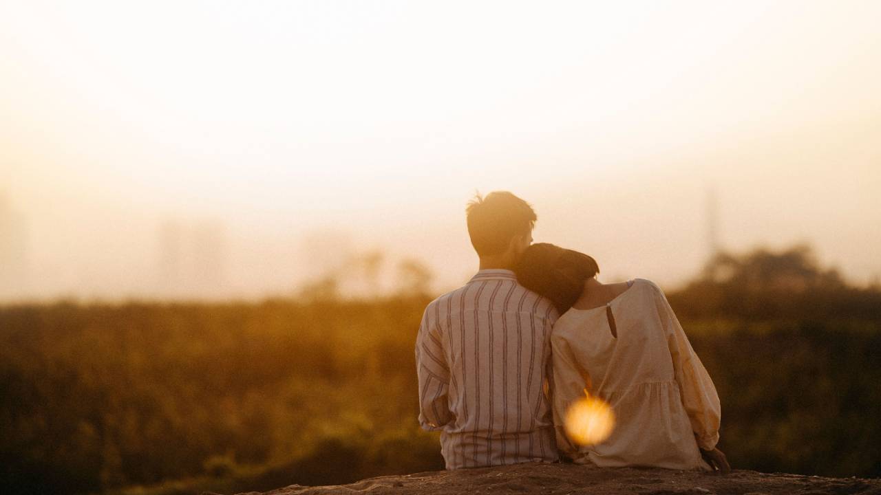 Couple sitting together in a field, with the woman resting her head on her husband’s shoulder