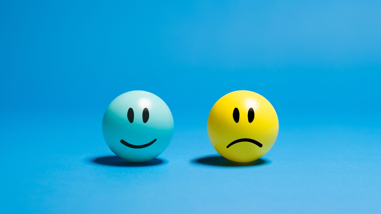 Happy and sad face icons against a blue background symbolizing emotions and emotional communication.