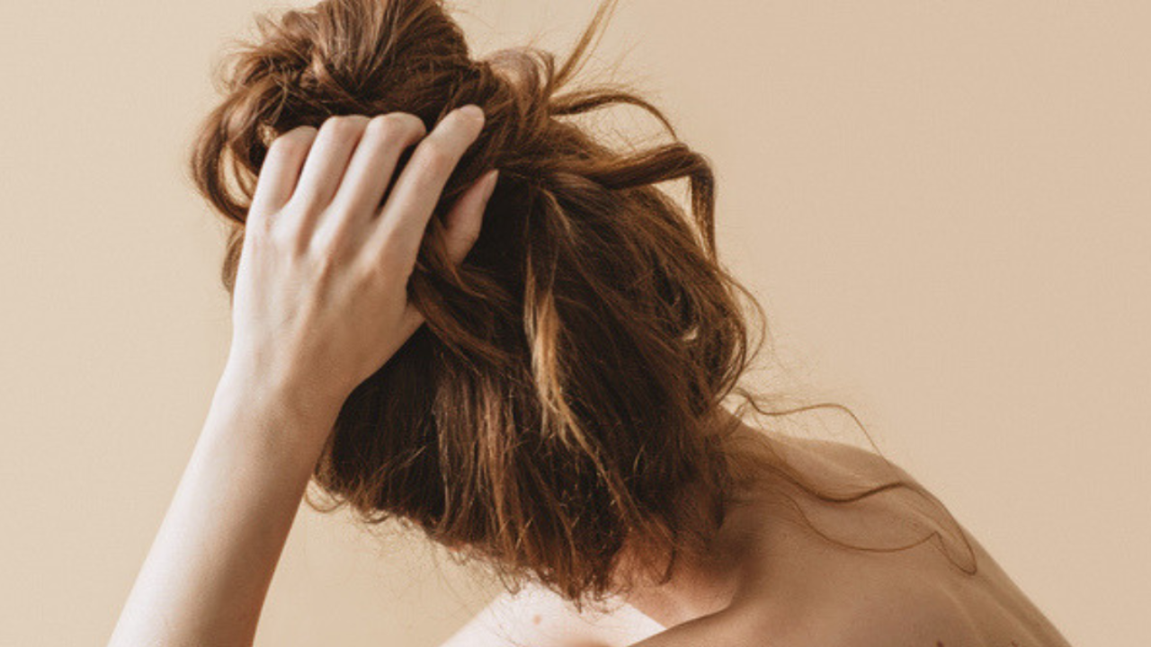 Woman gathering her auburn hair against a warm neutral background