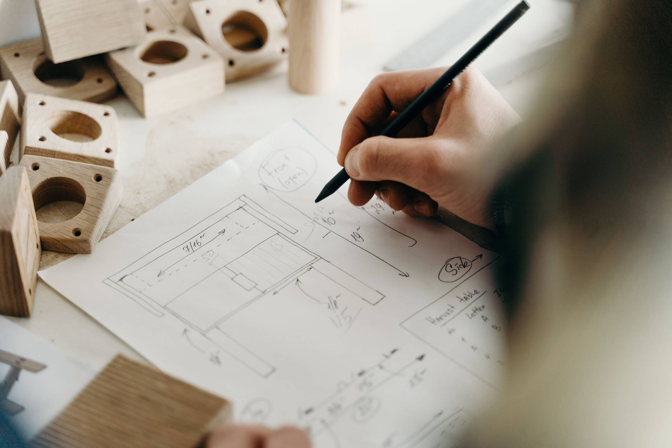 Person sketching a house floor plan beside architectural models