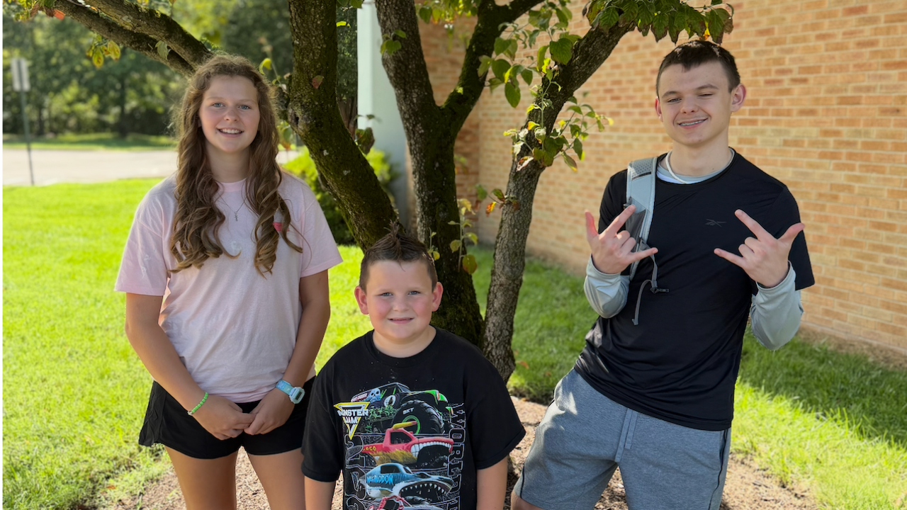 Three siblings smiling together on their first day of school.