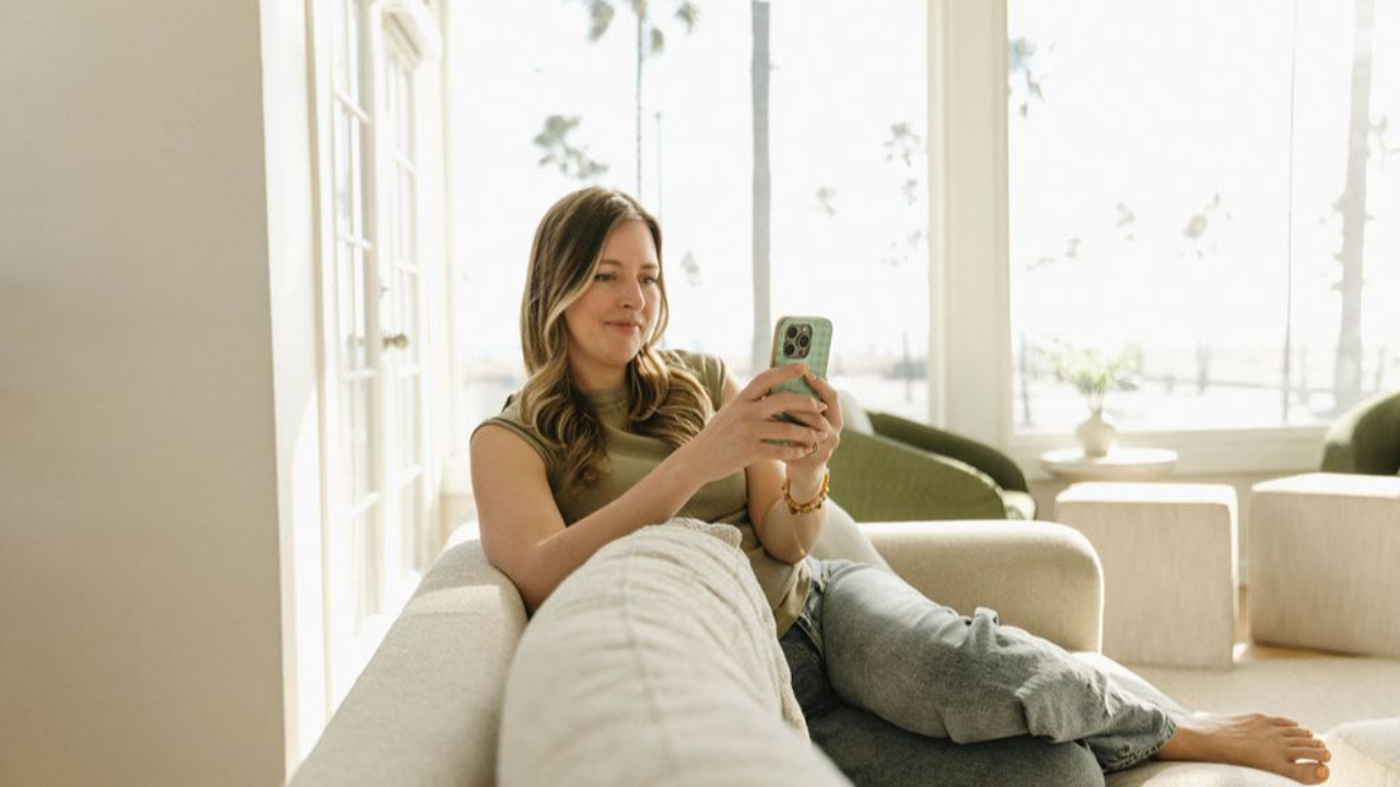 Image shows Julie Jones sitting comfortably on a couch writing a text on her iphone