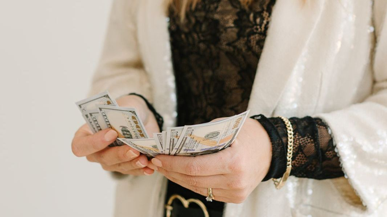 Image shows hands holding a stack of hundred dollar bills