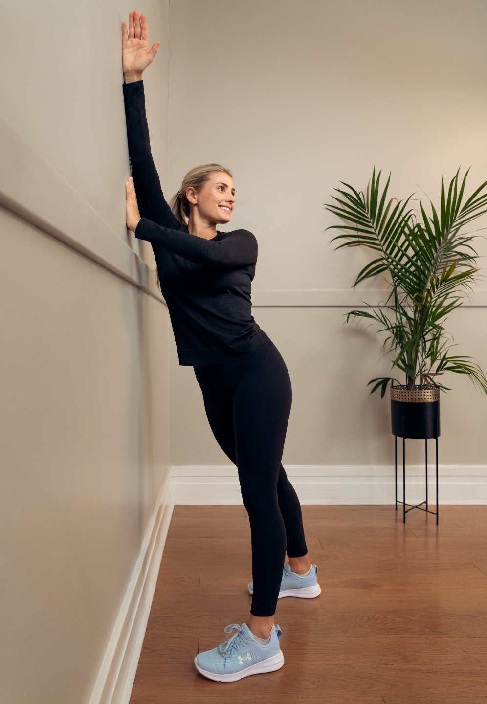 Woman stretching with the support of a wall, smiling.