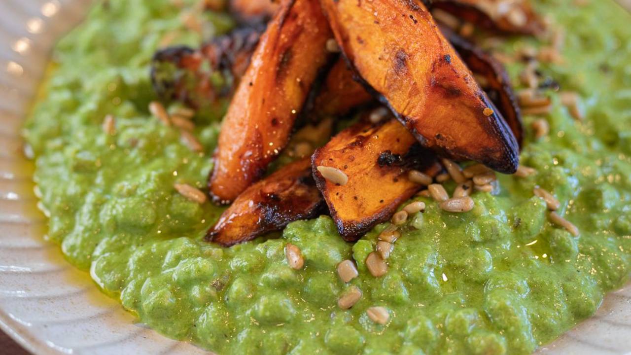 Bright green pearl barley risotto topped with charred honey roasted carrots and sunflower seeds