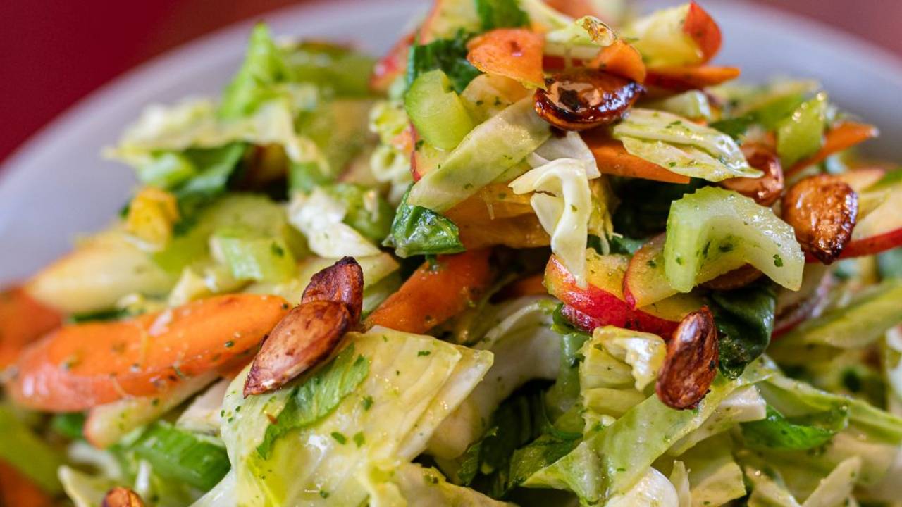 Fridge raid salad of thinly sliced celery, carrot, apple and cabbage in a bowl with a green herb stalk dressing