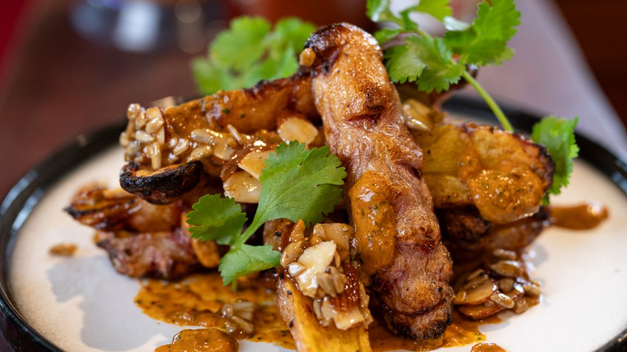 Roasted yams halved and caramelised on a serving board, topped with smoky piri piri sauce and scattered sweet spiced seeds and fresh coriander.