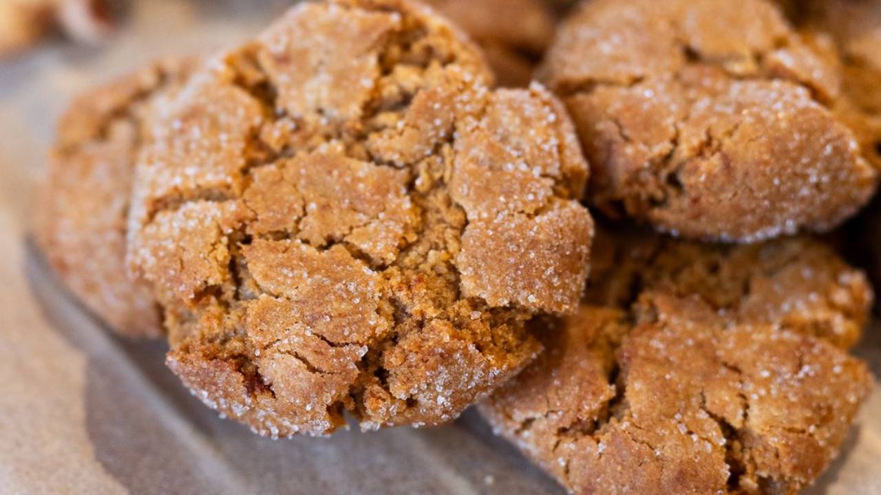 Dark cracked homemade gingernuts rolled in sugar, on baking paper on a wooden chopping board
