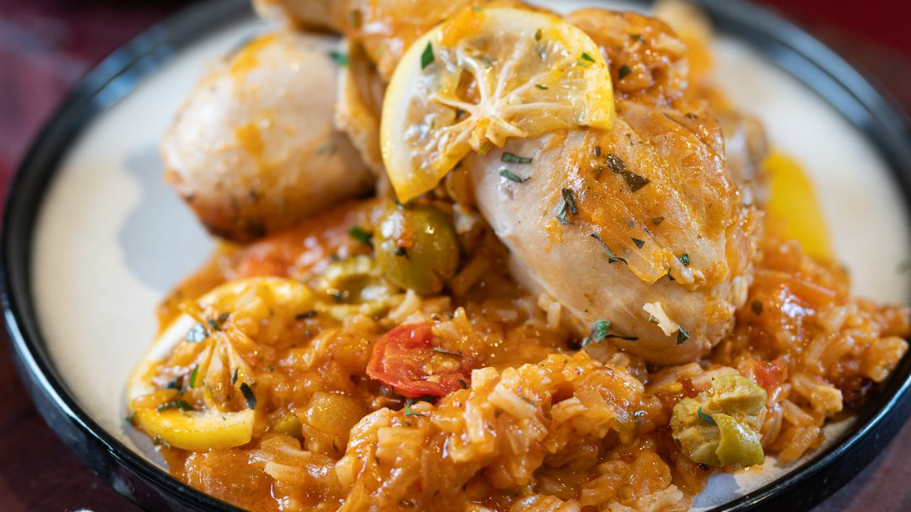 One pan peri peri chicken and rice with olives and lemon in a bowl, juicy chicken legs on top of saucy jasmine rice