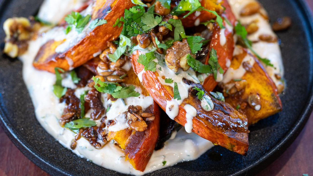 Roasted pumpkin half moons with sticky honey soy glaze on a bed of mint yoghurt topped with golden spiced nuts on a serving platter