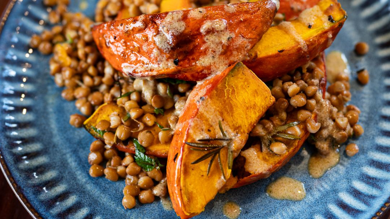 Roasted pumpkin half moons on a bed of herby brown lentils drizzled with tahini dressing on a serving plate