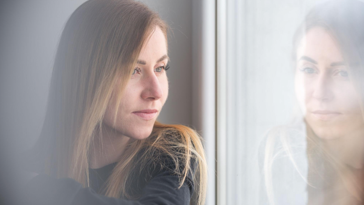 Woman sitting by a window looking thoughtful while reflecting on unexplained hormone symptoms, fatigue, weight gain and missing periods.