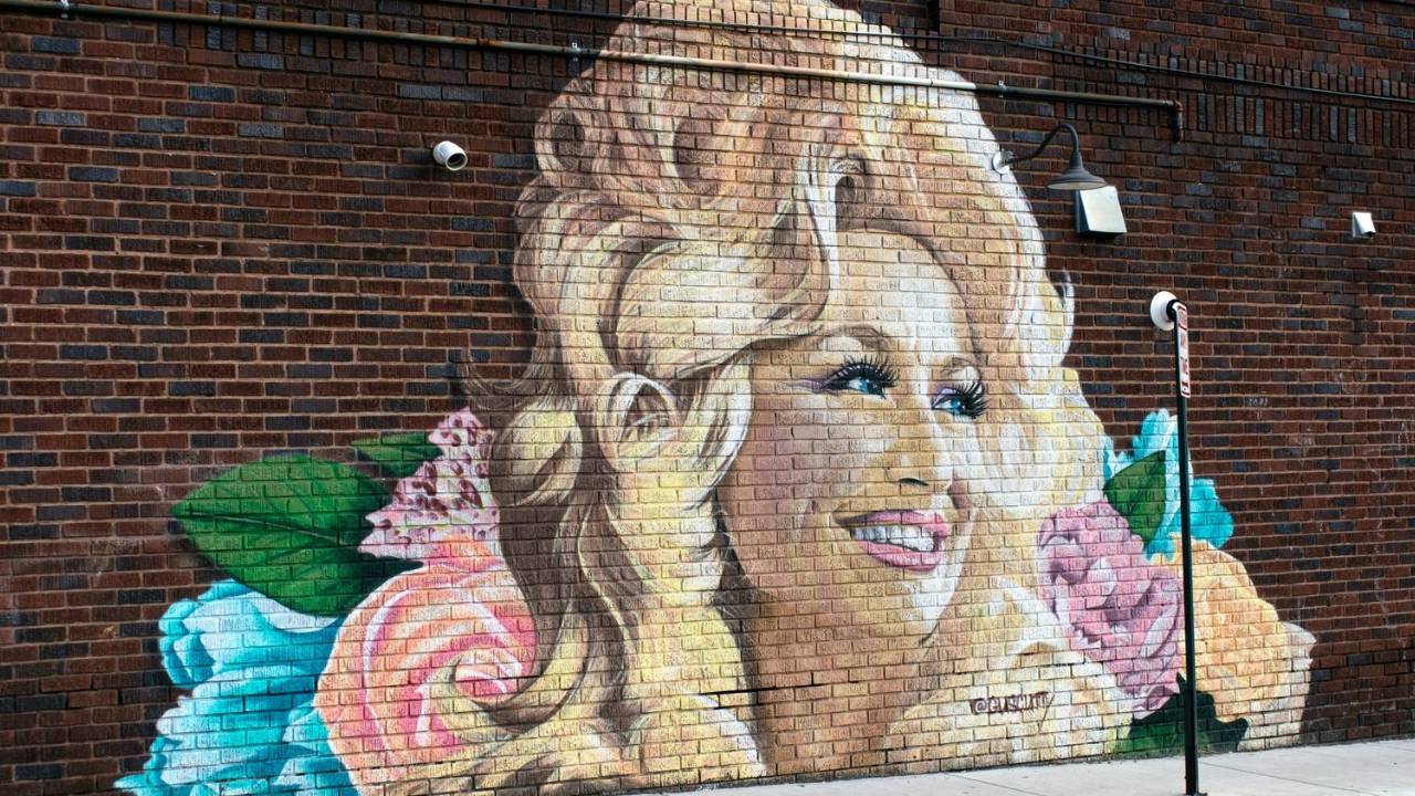mural of dolly parton with large blonde hair and a smile on brick wall 