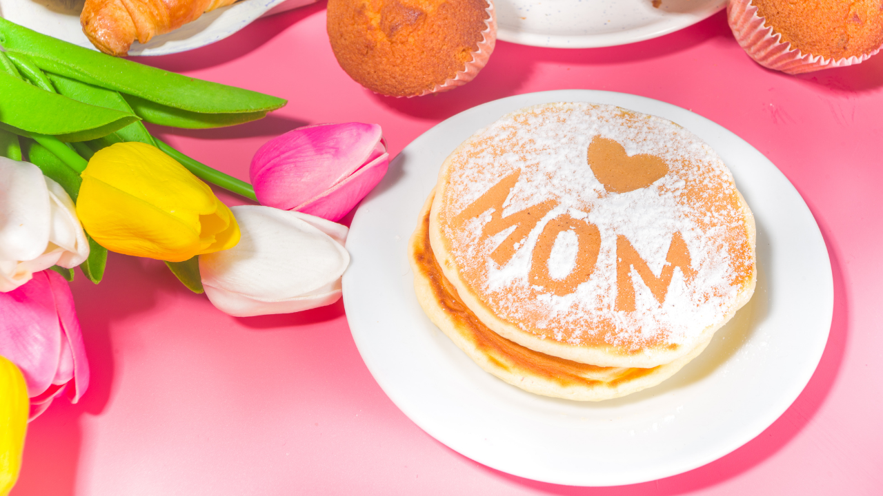 A mother's day brunch table set with flowers and pastries and pancakes with the word "mom" on top