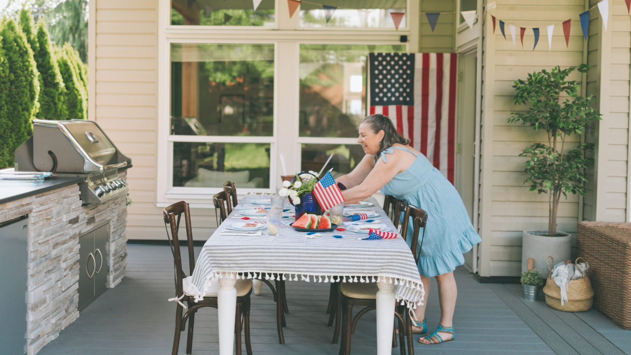 Woman setting up the outdoor dinner table with refreshments and 4th of July decor, getting ready to host the cookout