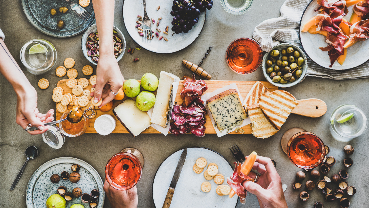 Friends getting together in the summer for a charcuterie style picnic filled with cheeses, crackers, fruits, dips, and wine