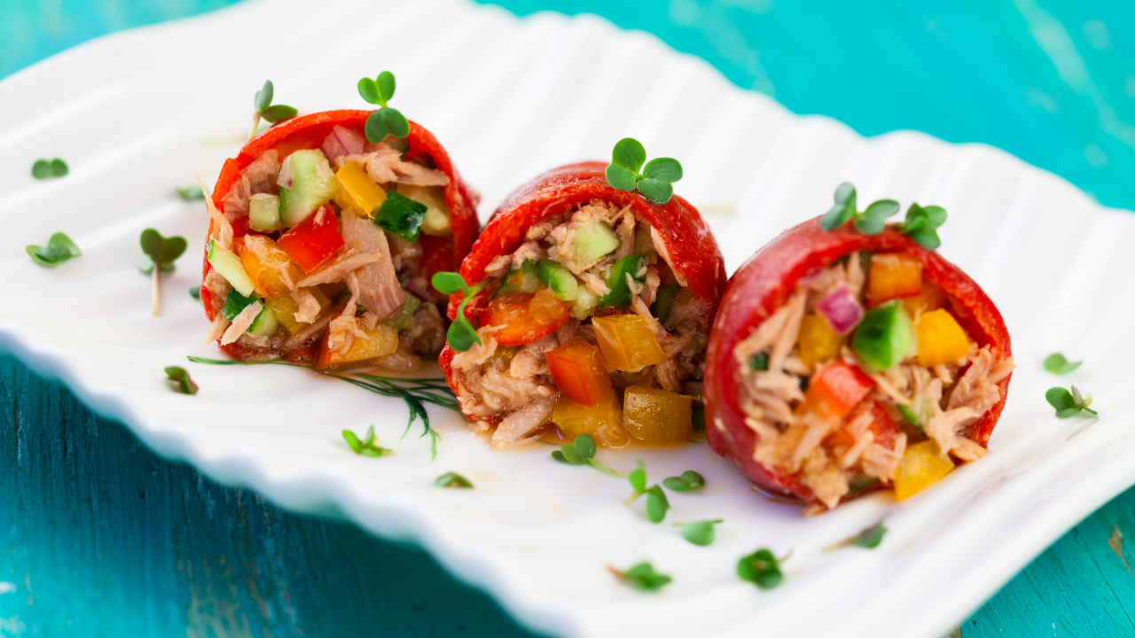 tuna salad packed with healthy fats and protein, stuffed into naturally sweet red bell peppers plated on a white serving platter and garnished with fresh herbs
