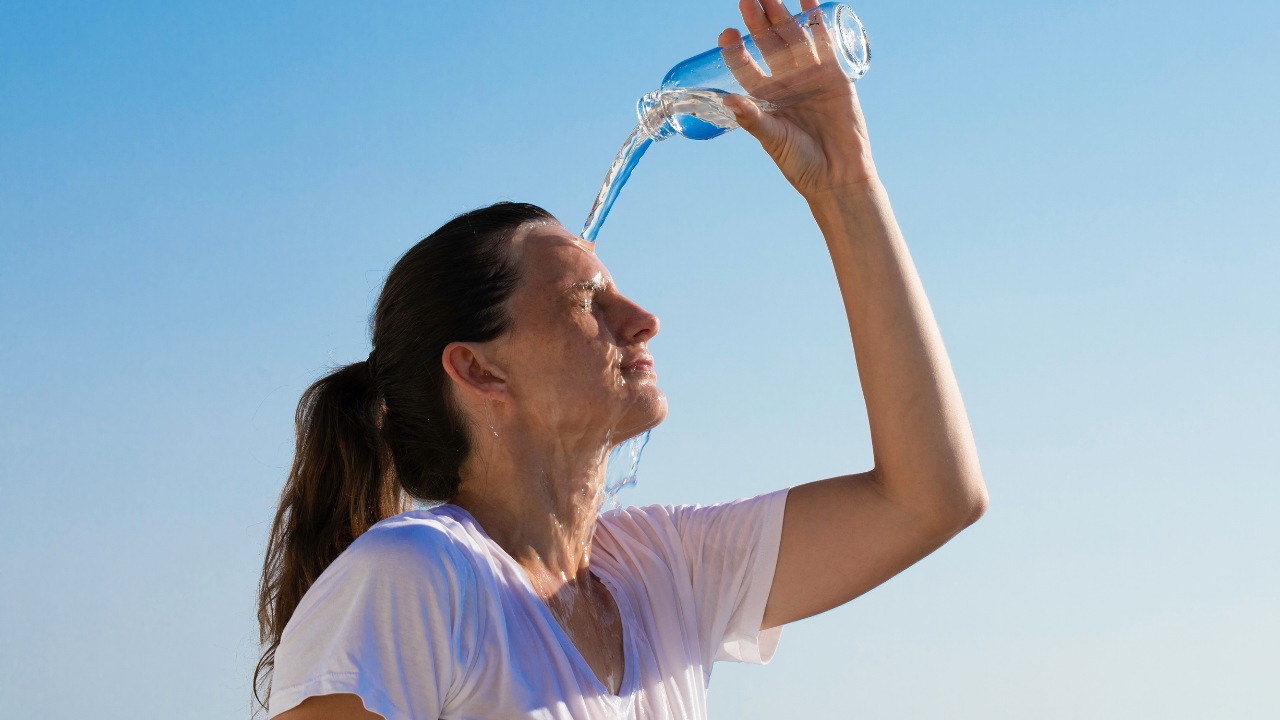 Woman on a hot summer day in the sun, pouring water on her face