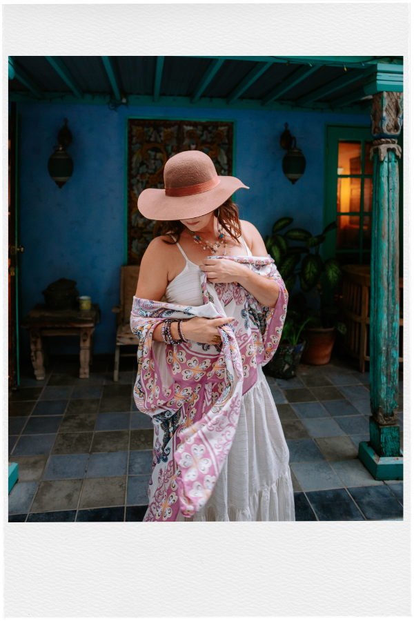 Ashley Levin Wearing a White Dress with a Hat Looking Down with a Pink Scarf