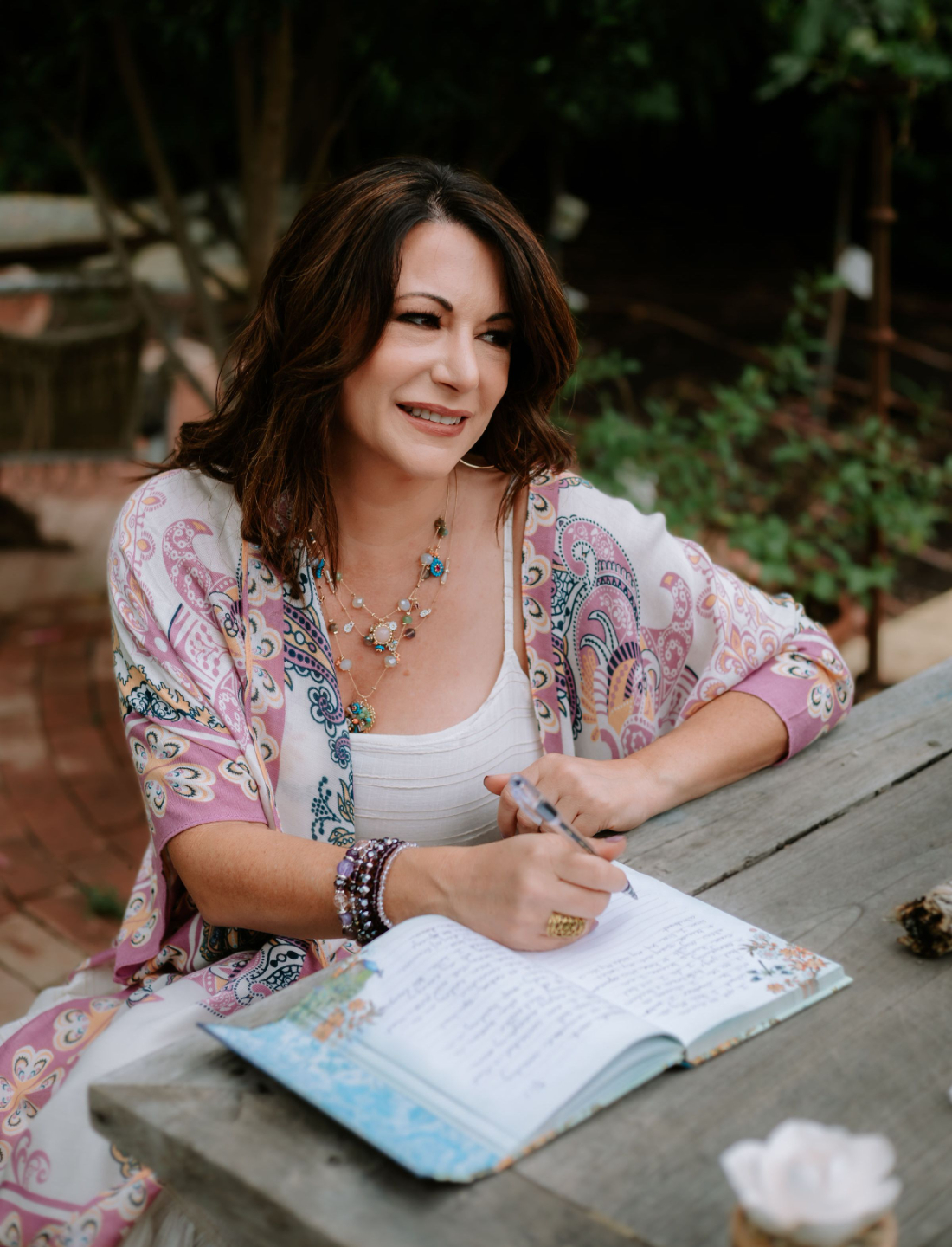 Ashley Levin Sitting on a Wood Bench with a Jounral and Pen and smiling away from the camera