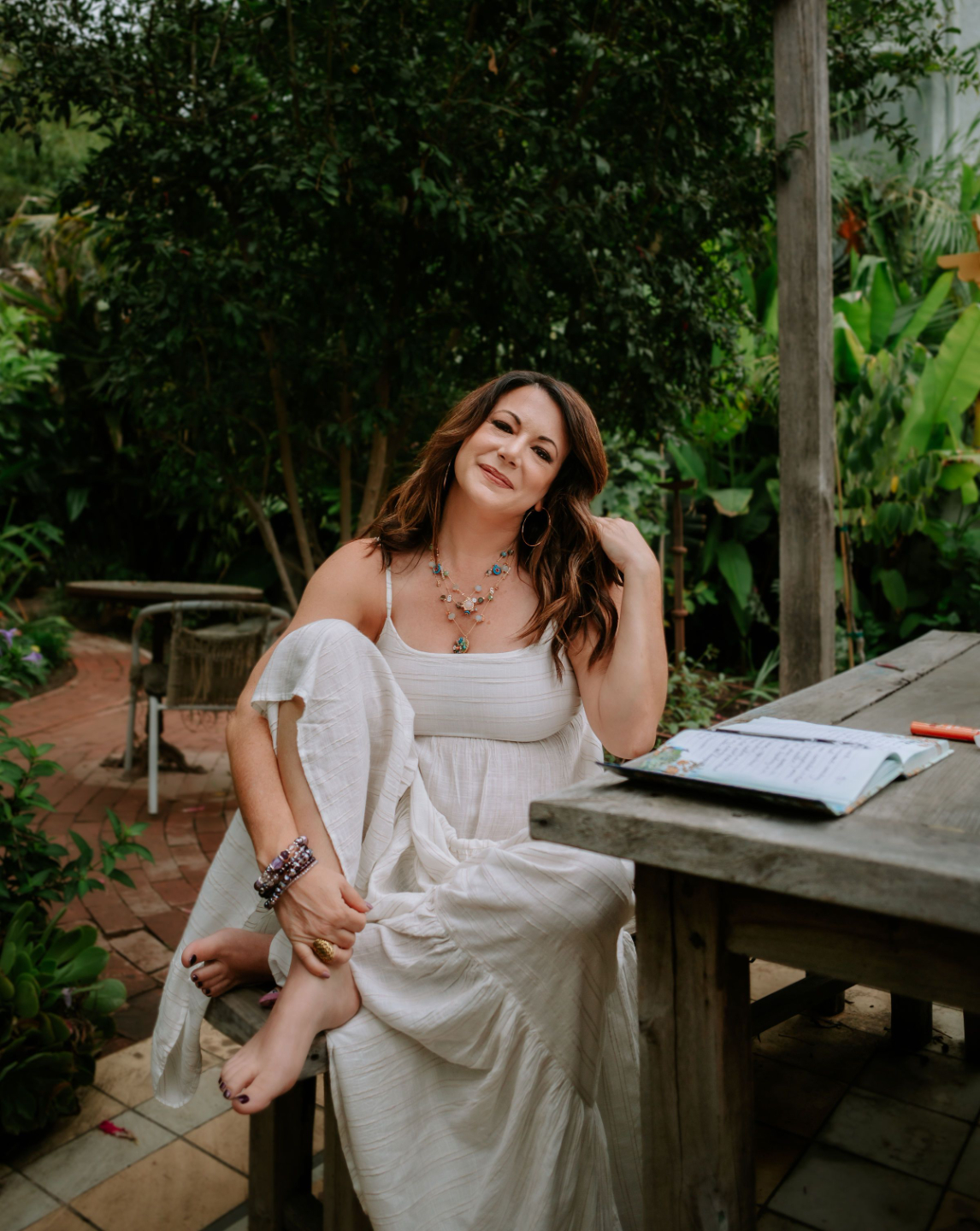 Ashley Levin Sitting on Wood Bench, Wearing a White Dress and Looking at the Camera