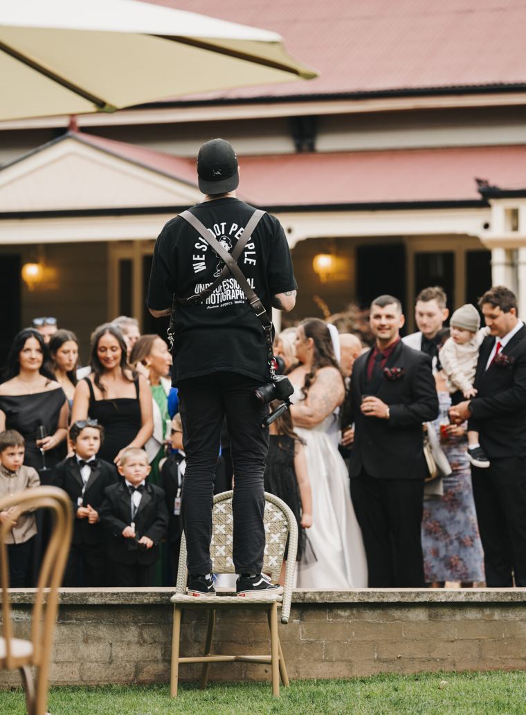 Josh standing on a chair photographing a wedding crowd