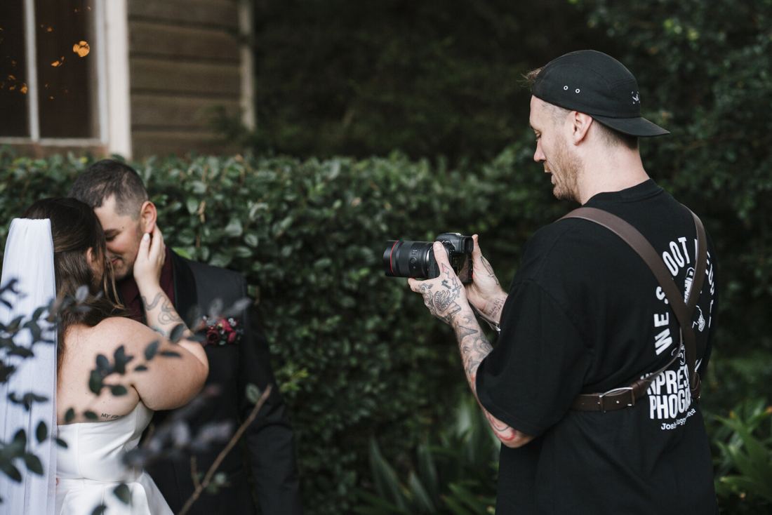 Josh photographing a couple up close beside a hedge