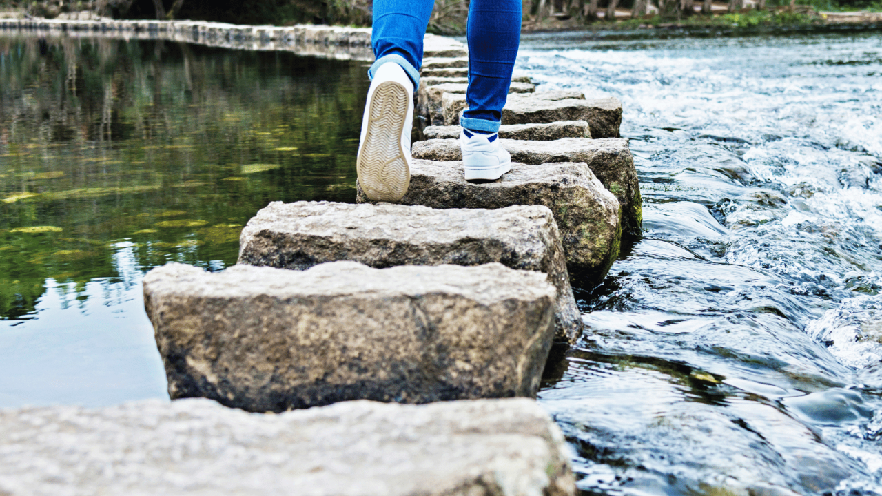 Person walking on stepping stones across water representing the phases of rebuilding trust after betrayal