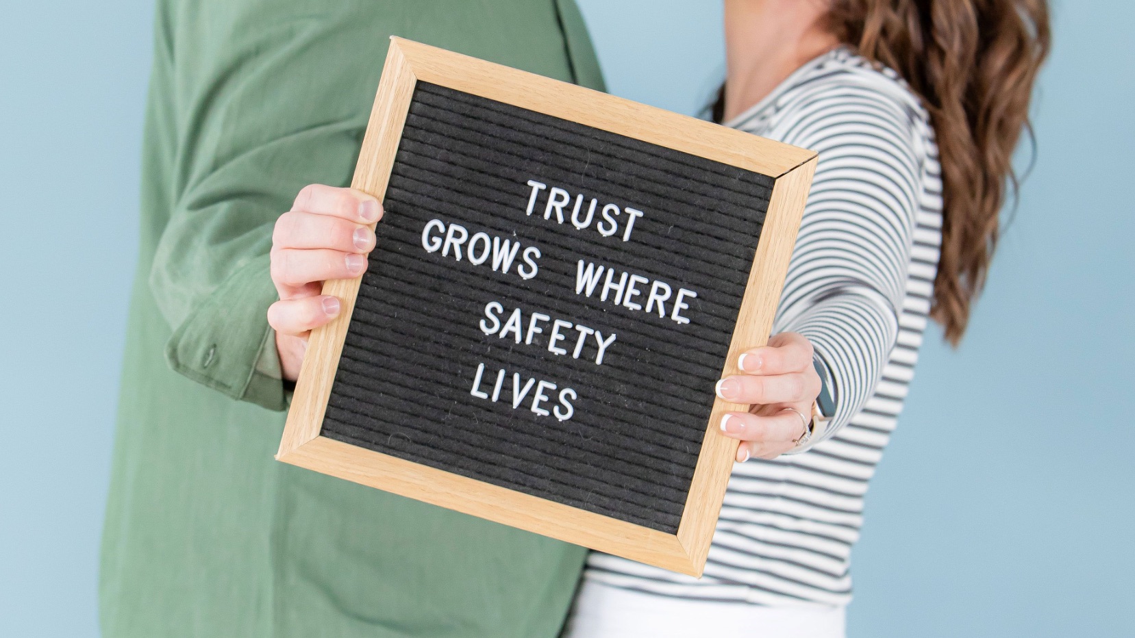 Couple holding a sign that says "Trust Grows Where Safety Lives"