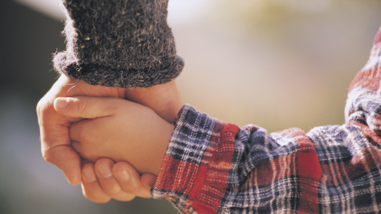 A close-up of a parent and child's hands together, conveying connection, trust, and the ongoing work of keeping someone safe.
