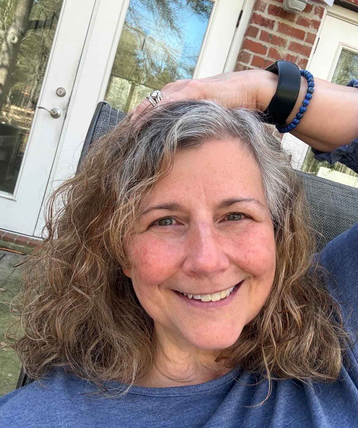Woman smiling at the camera, her left hand resting on the top of her head in a laid-back manner