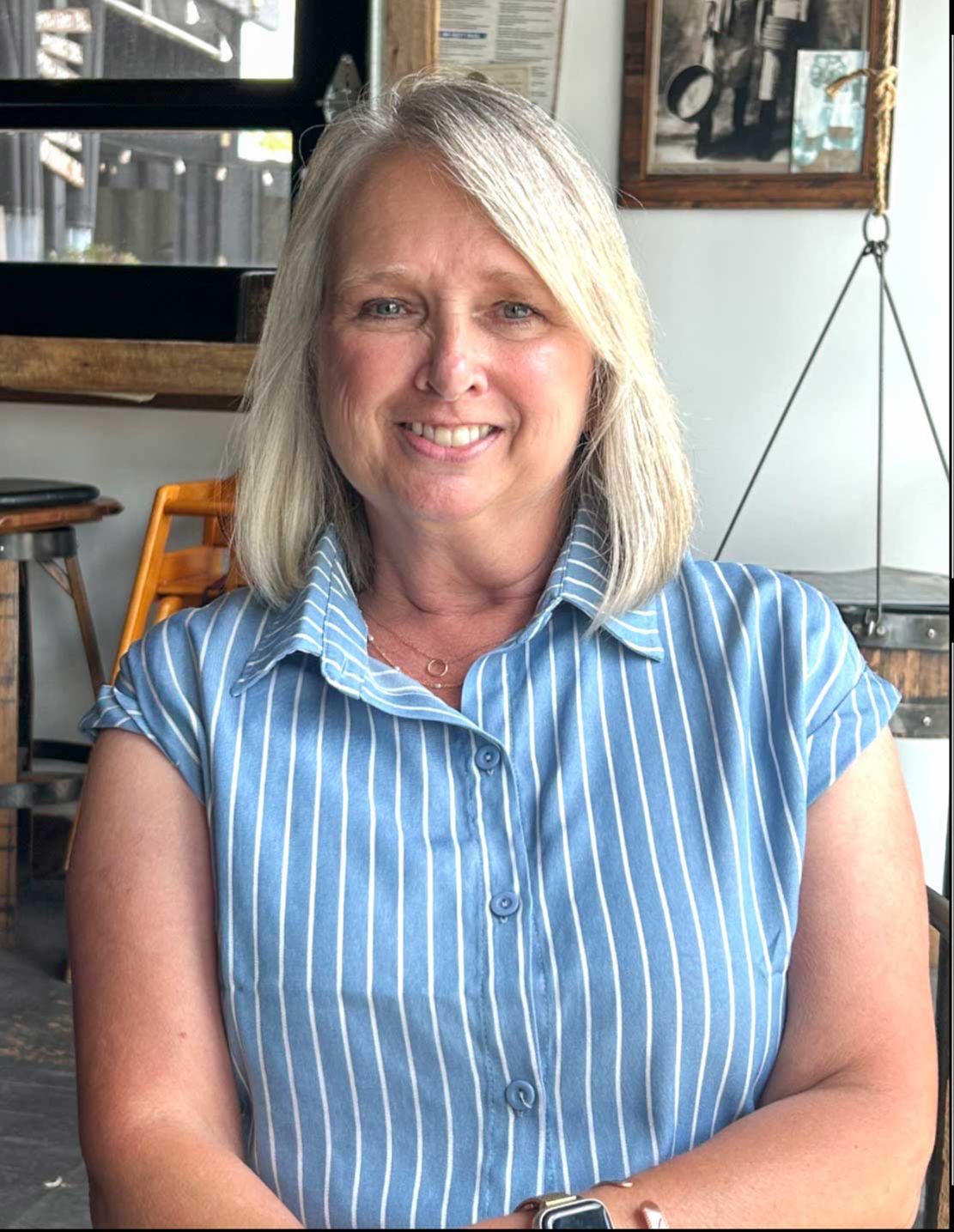 Blond-haired woman in a blue and white, striped button down shirt, smiling at the camera.