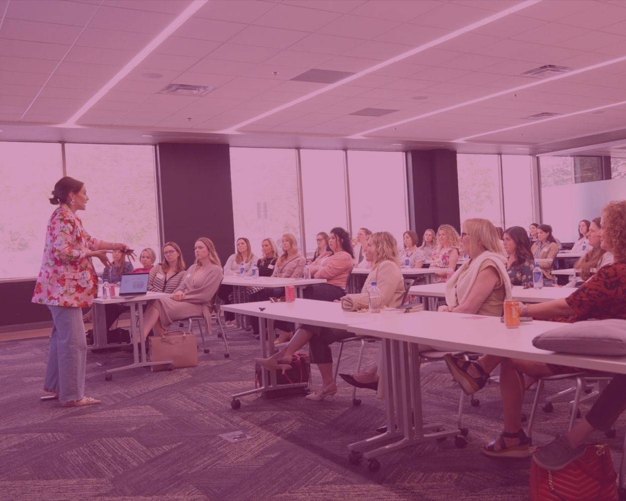 Tiffany Sauder teaching at the front of a bright room as rows of women seated at long tables listen.