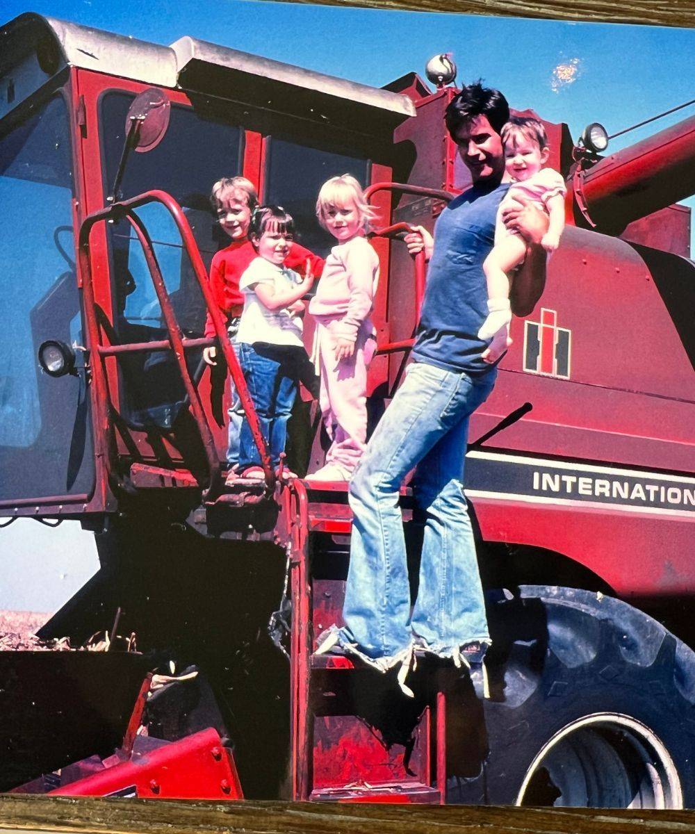 A young Tiffany with her dad and her three siblings on the steps of a red combine.
