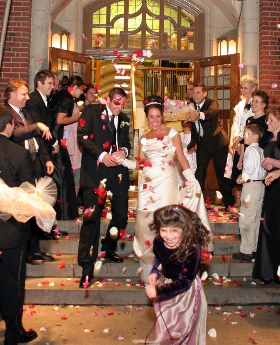 Tiffany and JR leaving their wedding through a shower of rose petals, with a flower girl running ahead.
