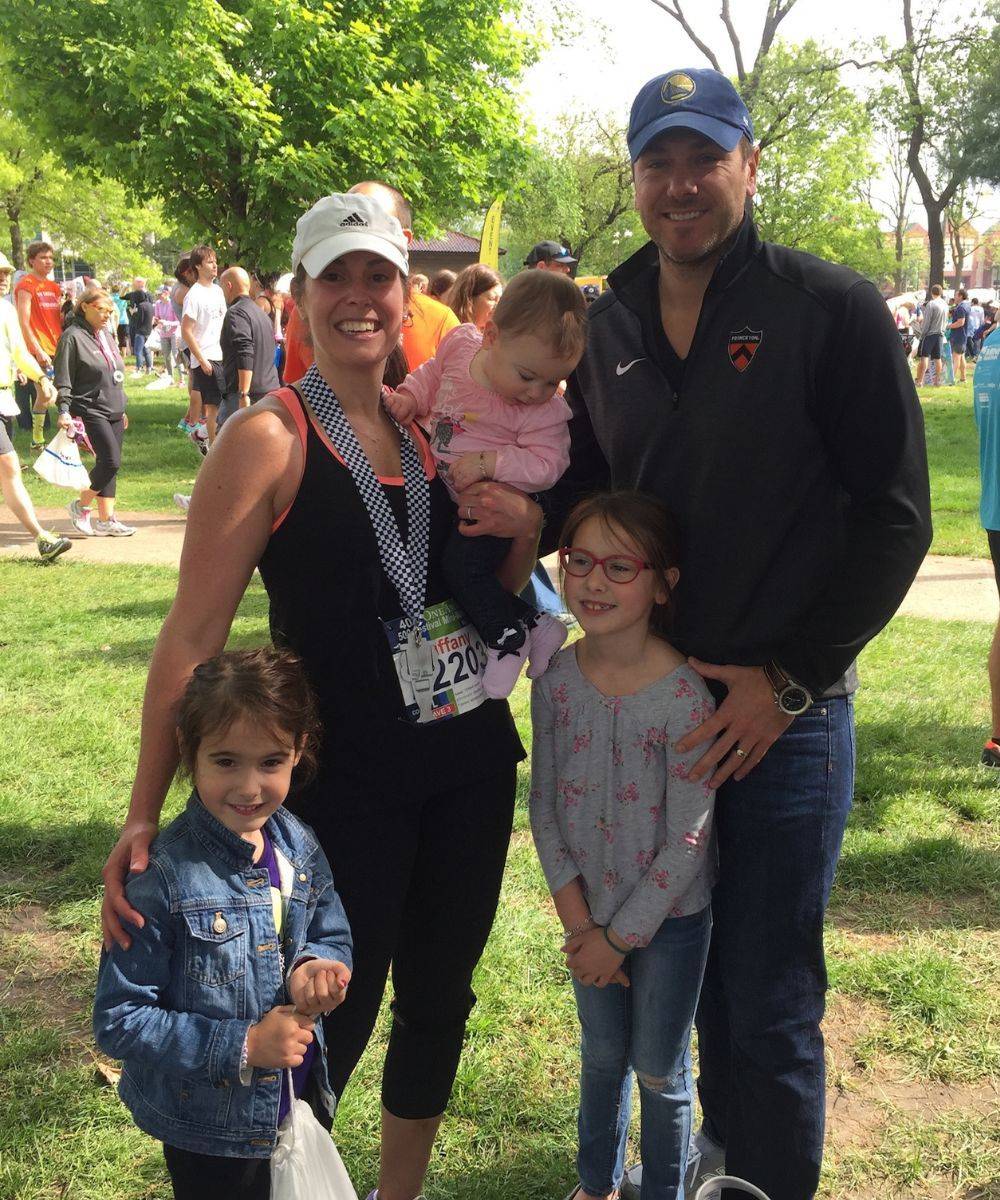 Tiffany wearing a race medal, with JR and their young daughters at the finish line.