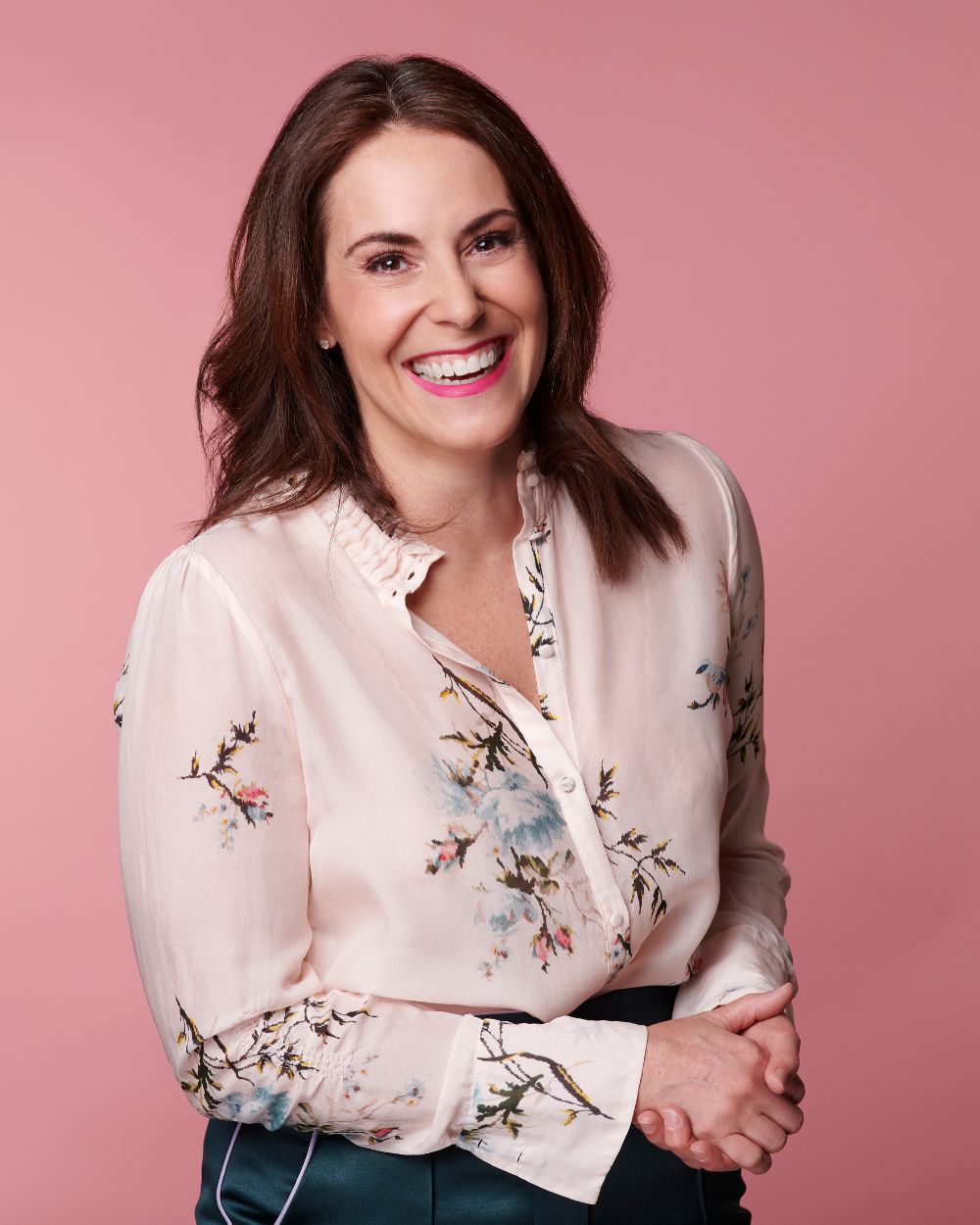Tiffany Sauder smiling in a cream floral blouse against a pink backdrop