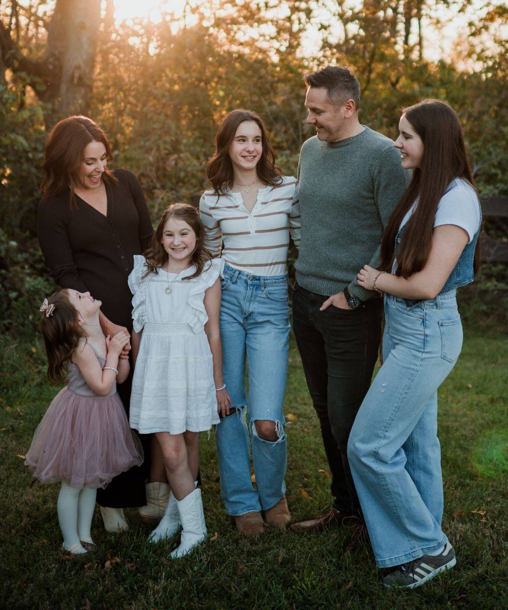 Tiffany and JR with their four daughters, outdoors at sunset.