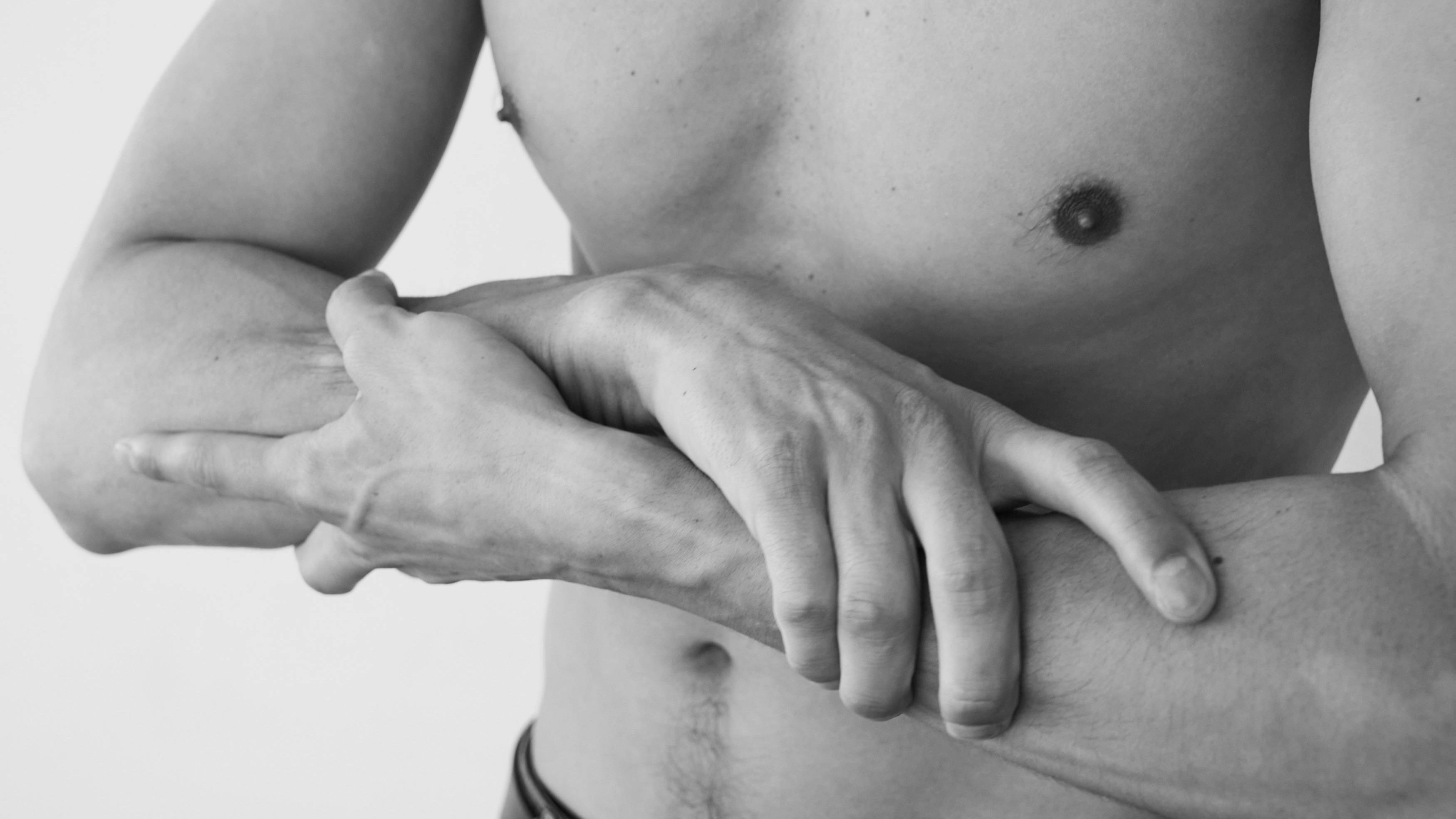 Visualising somatic presence and intentionality in solo intimacy: A masculine body holding their own forearms, symbolising the practice of slowing down self-pleasure to deepen body connection and sensory awareness, explored at Intimata Oxford.